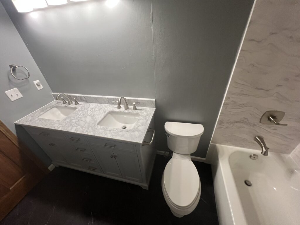 Full bathroom remodel with Carrara-look walls and gray double vanity