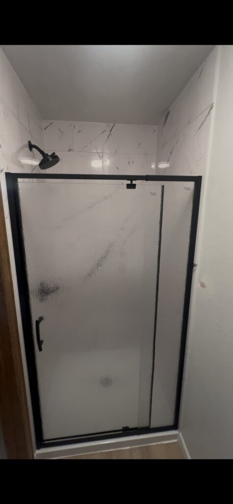 Walk-in shower conversion with matte black framed glass and grout-free wall panels